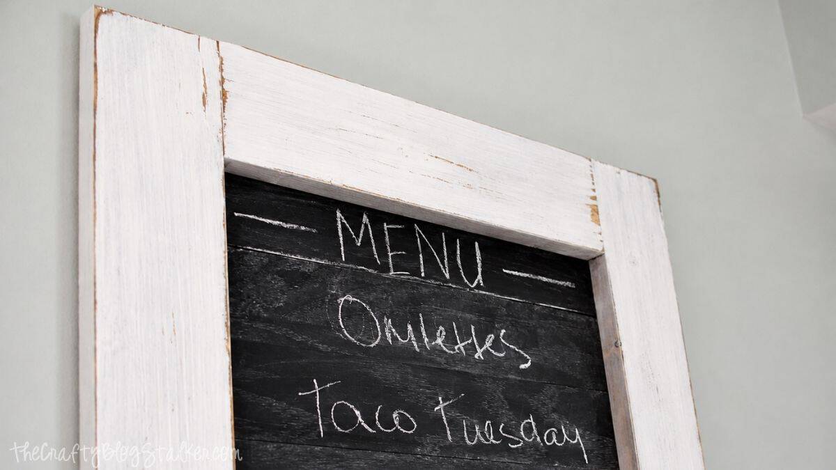 Is the family always asking what's for dinner? Create this super cute planked Kitchen Chalkboard Menu to keep them up to date! Click through for the tutorial on how to make this chalkboard menu! Close-up of a rustic framed chalkboard menu with a distressed white wood frame and handwritten meal ideas in white chalk.