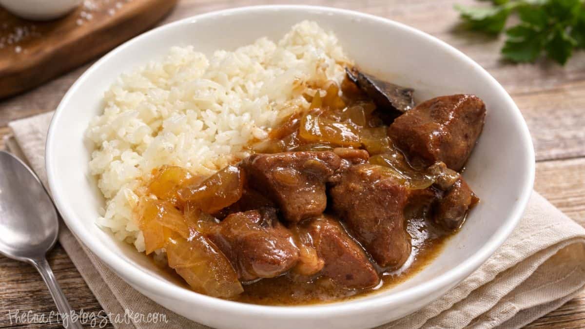 Bowl of slow cooker beef tips in rich gravy served over fluffy white rice on a rustic table setting.