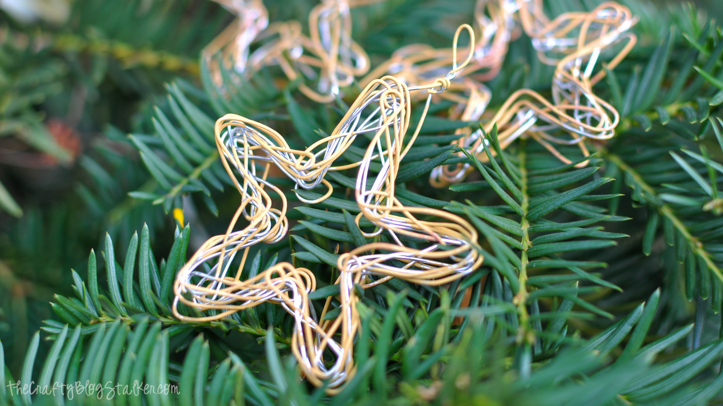 How to make Wire Star Ornaments. Such a fun and easy handmade ornament! Handmade wire star ornaments in gold and silver resting on green evergreen branches.