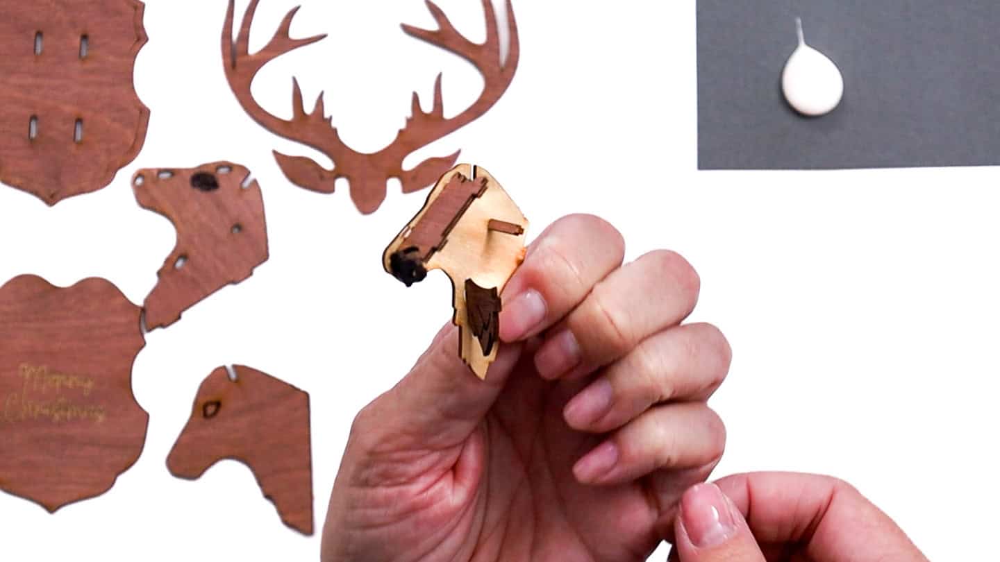 A hand holding a partially assembled wooden reindeer ornament piece, with other laser-cut reindeer parts spread out on the table.