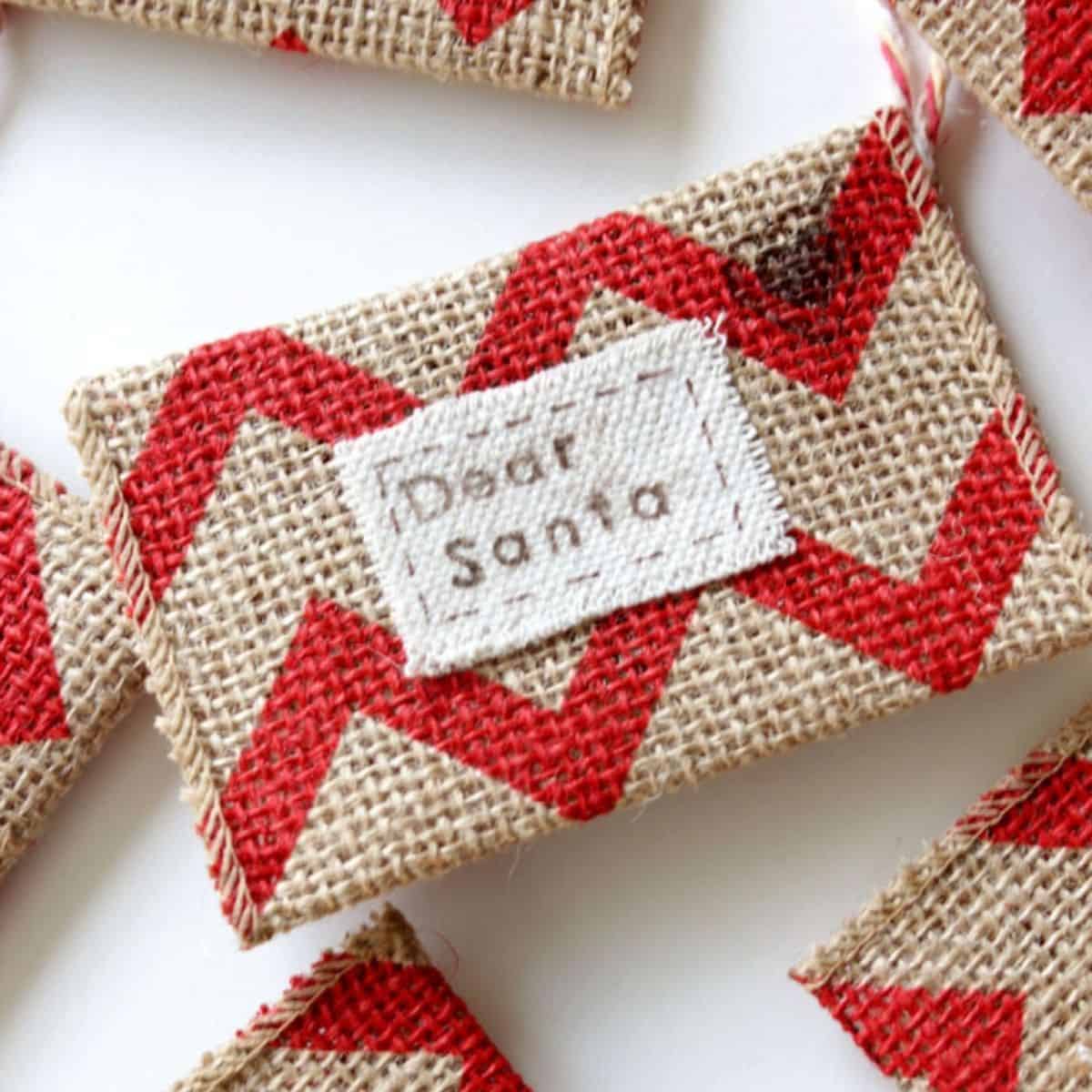 Small burlap envelope ornament with a red chevron pattern and a stitched fabric label that reads