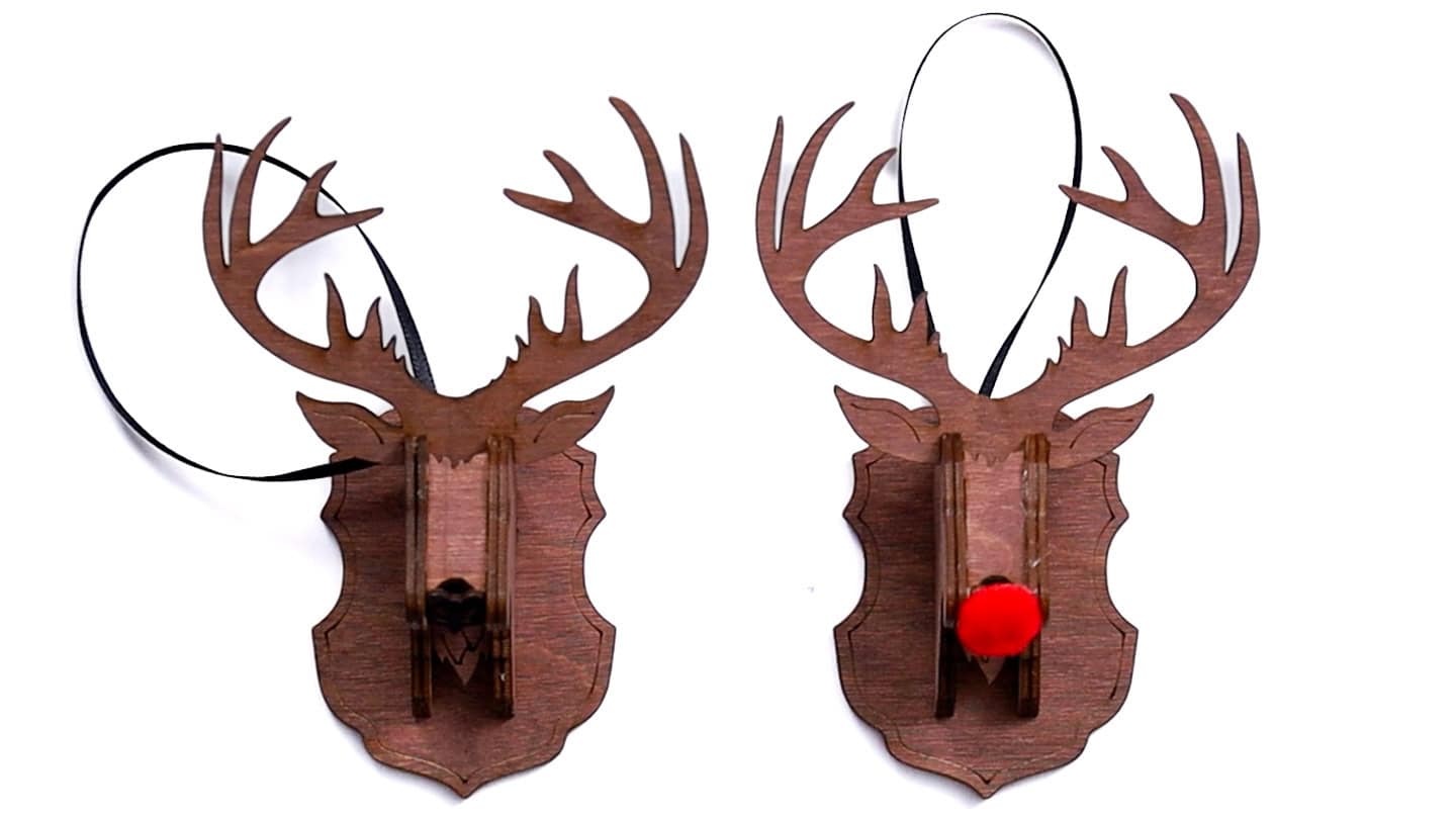 Two finished wooden reindeer head ornaments with antlers, one with a black nose and one with a red pom-pom nose, each hanging from a black ribbon.