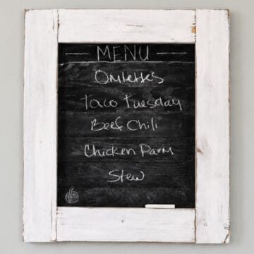 Rustic framed chalkboard menu board hanging on a gray wall with a distressed white wood frame and handwritten weekly dinner ideas.