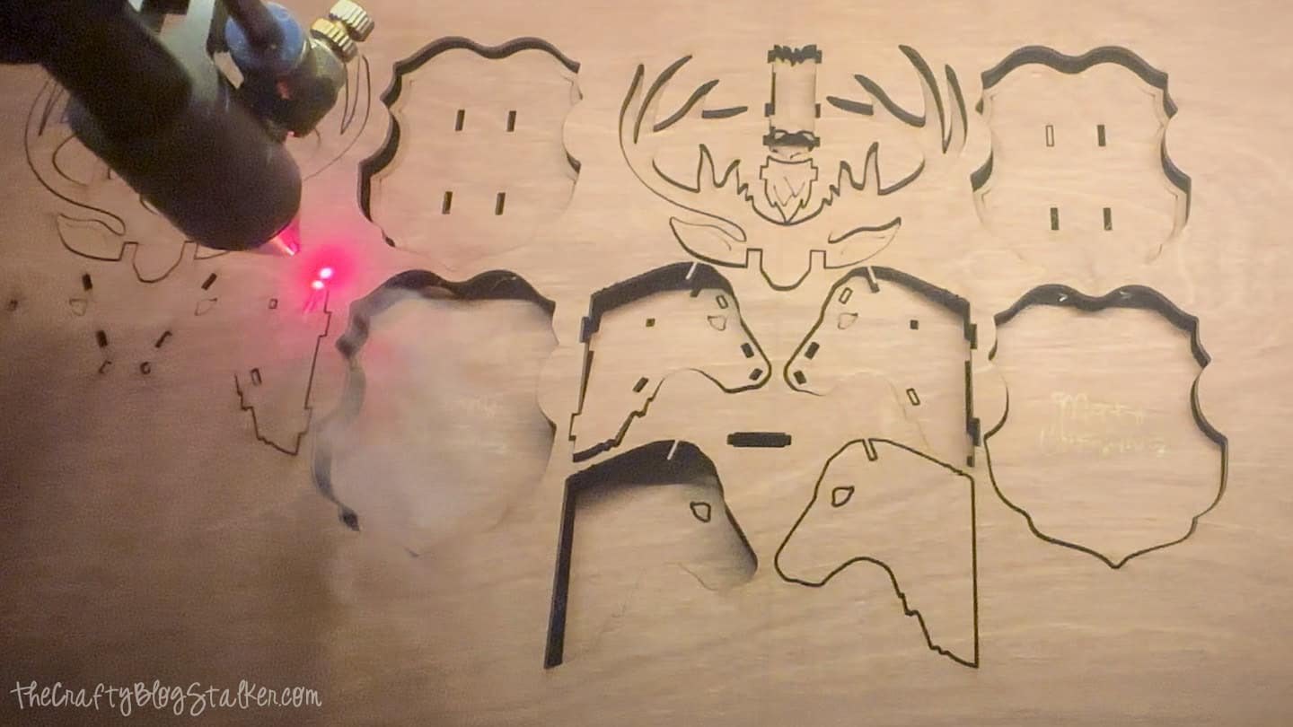 Laser cutter etching reindeer ornament pieces into a stained wood board, with a red guide light marking the cut lines.