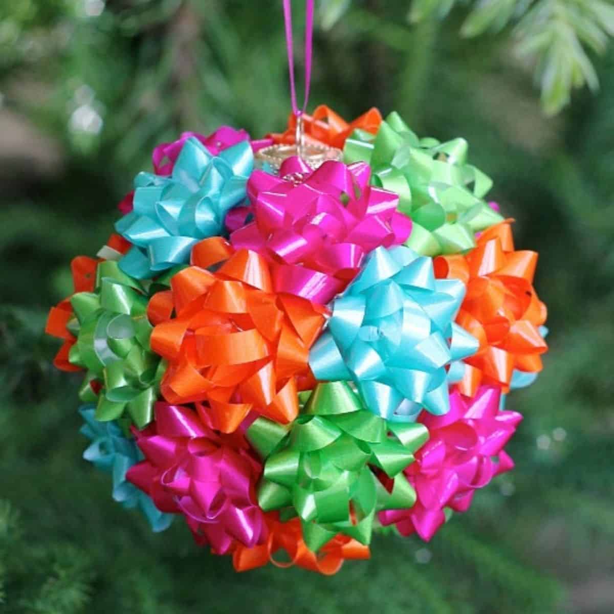 Colorful Christmas ornament made from bright mini gift bows in pink, blue, green, and orange hanging on a tree.