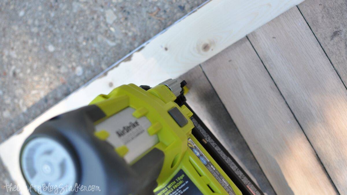 Close-up of a nail gun securing wood slats to the back of an unfinished wooden frame during chalkboard assembly.