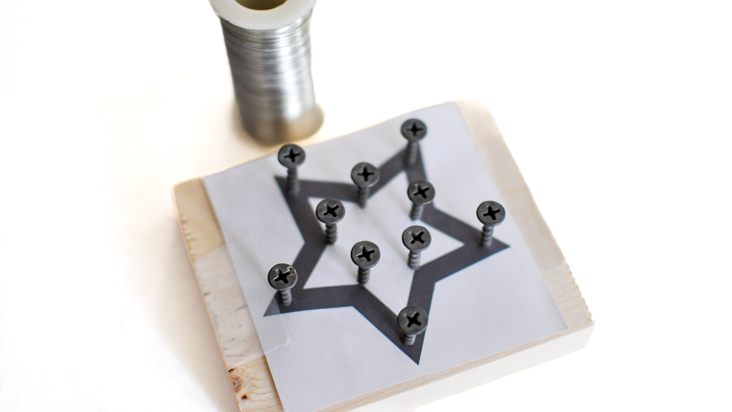 A wood block with a printed star template and screws placed along the outline, with a spool of wire sitting nearby for the ornament craft.
