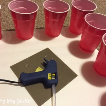 Using hot glue to stick red plastic cups to the foam core boards.