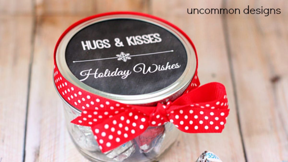 Mason jar filled with chocolate treats, tied with a red polka dot ribbon and topped with a Hugs & Kisses Holiday Wishes printable tag.