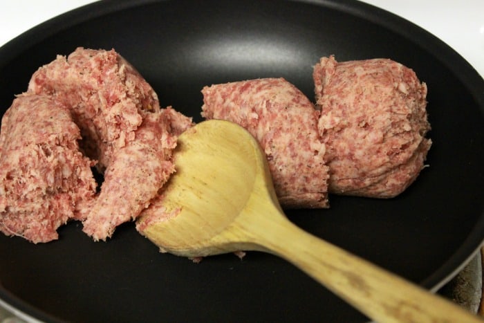 Cooking sausage in a frying pan with a wood spoon.