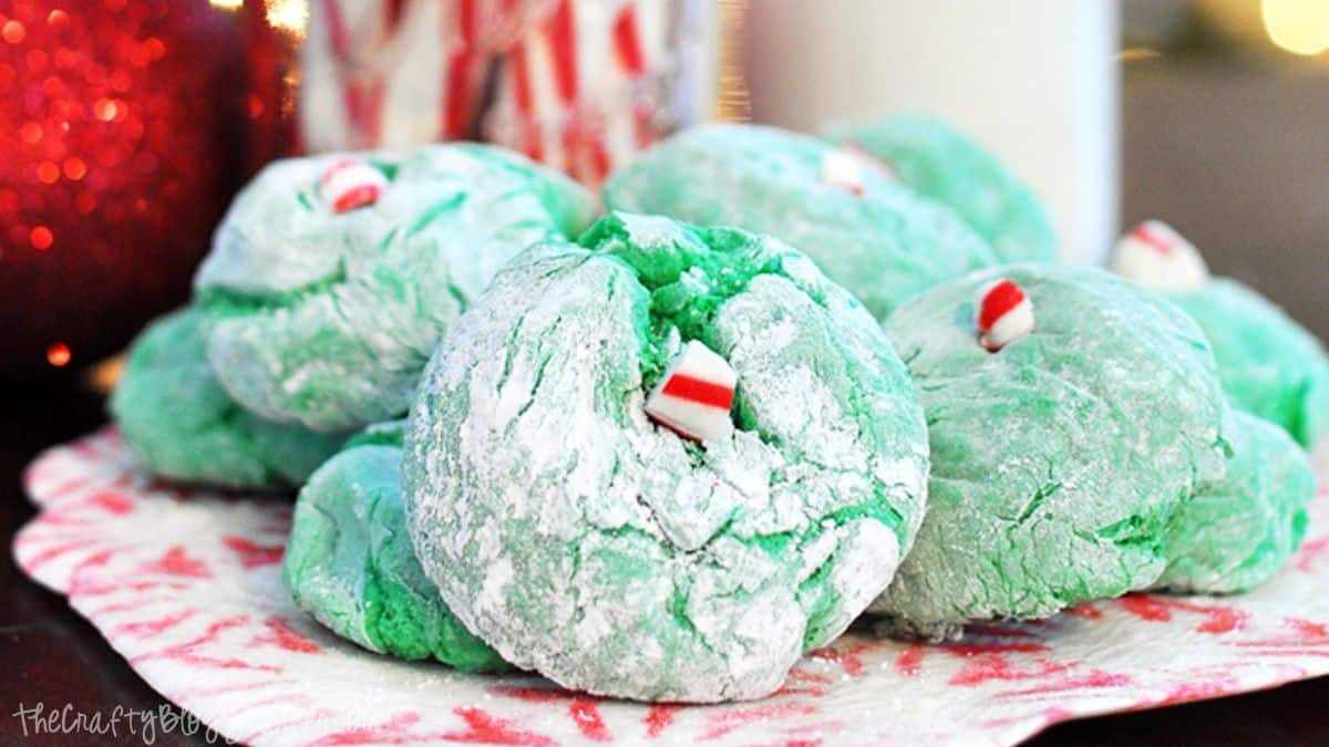 Green crinkle cookies dusted with powdered sugar and topped with small peppermint candy pieces, displayed on a festive holiday plate.