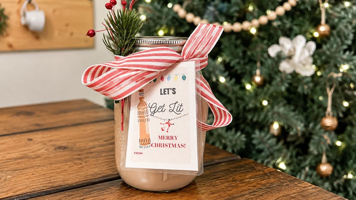 Mason jar of homemade Irish cream tied with red striped ribbon, greenery, and a “Let’s Get Lit” Christmas gift tag beside a decorated tree.