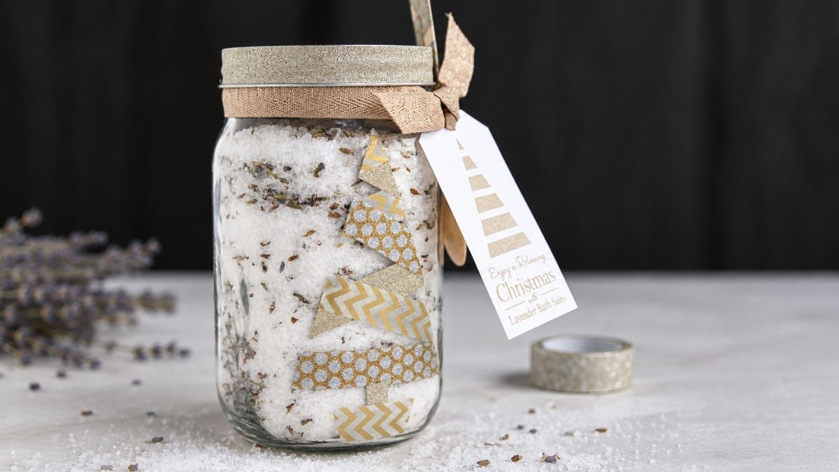 Mason jar filled with lavender bath salts, decorated with gold patterned tape, ribbon, and a Christmas gift tag.