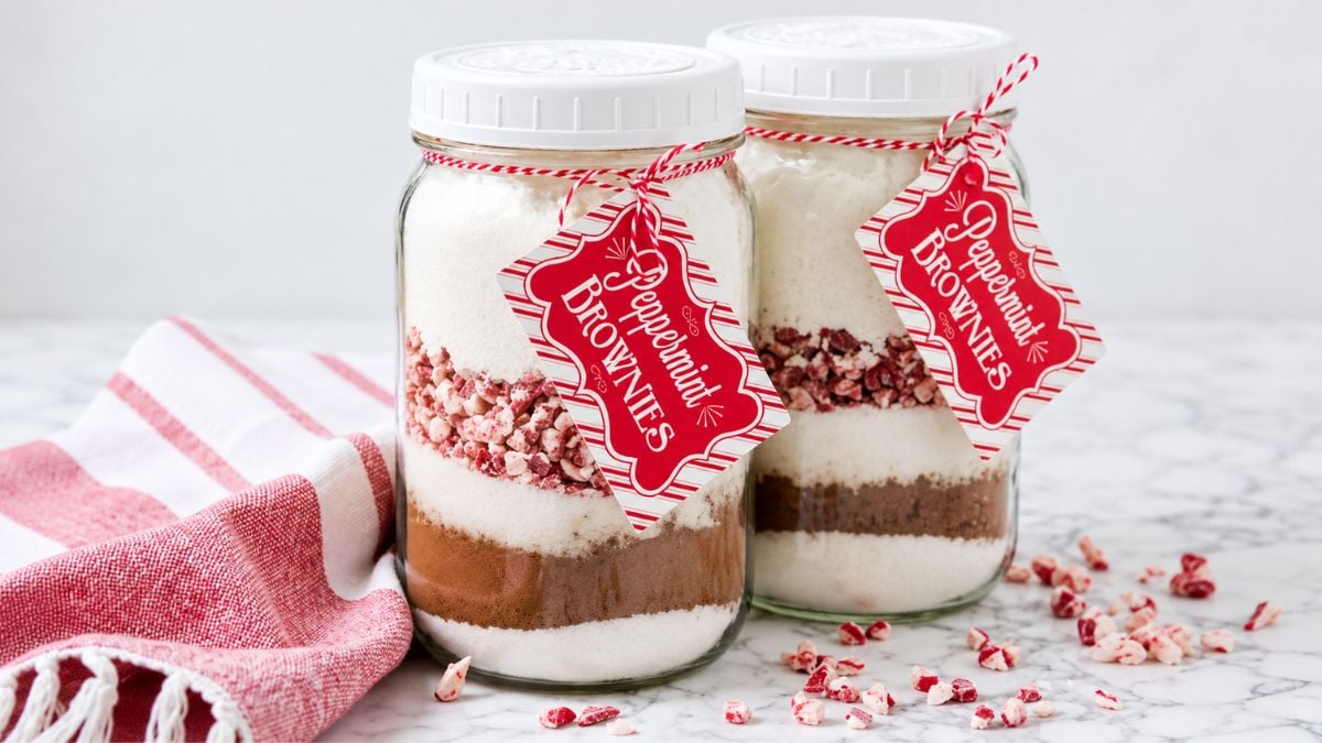Two mason jars layered with peppermint brownie mix ingredients, tied with red and white twine and festive Peppermint Brownies gift tags.