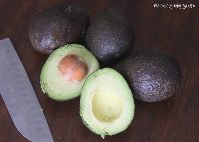 Four avocados, one has been sliced in half with a sharp knife.
