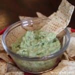 A tortilla chip that has been dipped in a bowl of guacamole dip.