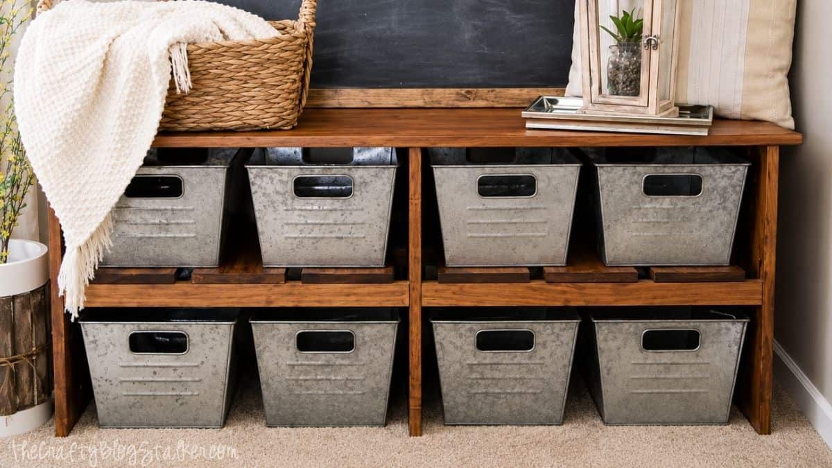Wood storage bench with open shelves and galvanized metal bins, styled with blankets, pillows, and farmhouse decor.