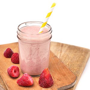 Delicious pink strawberry smoothie served in a mason jar with a yellow-striped straw, surrounded by fresh strawberries on a wooden board.