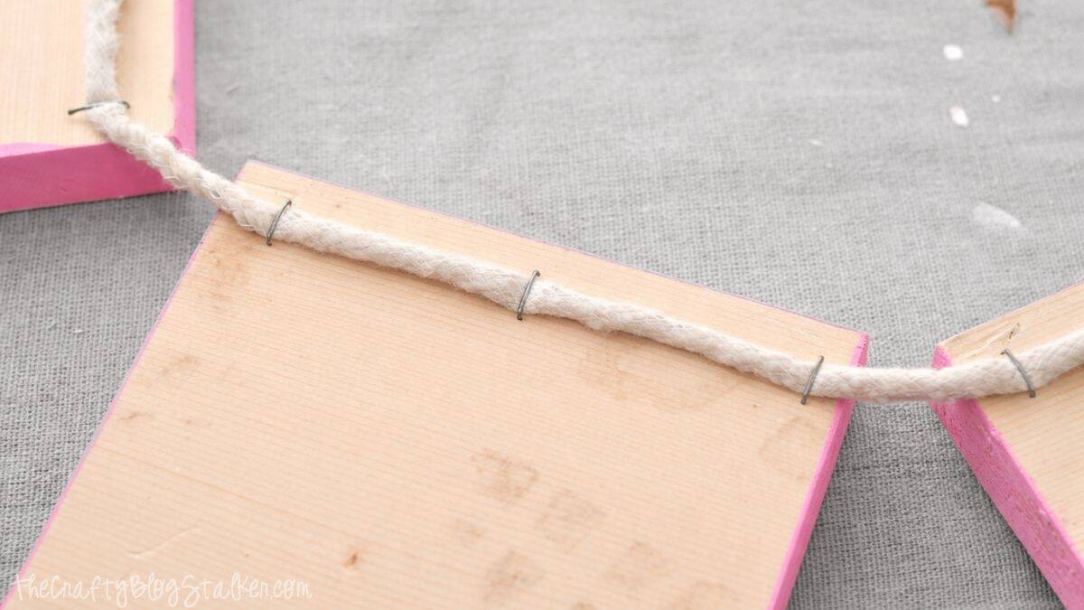 Close-up of rope stapled to the back of wooden banner squares, showing how the pieces are connected to create a hanging DIY banner.