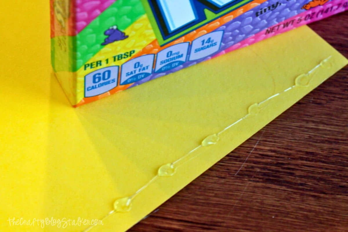 Applying Hot glue in dots on a sheet of yellow cardstock.