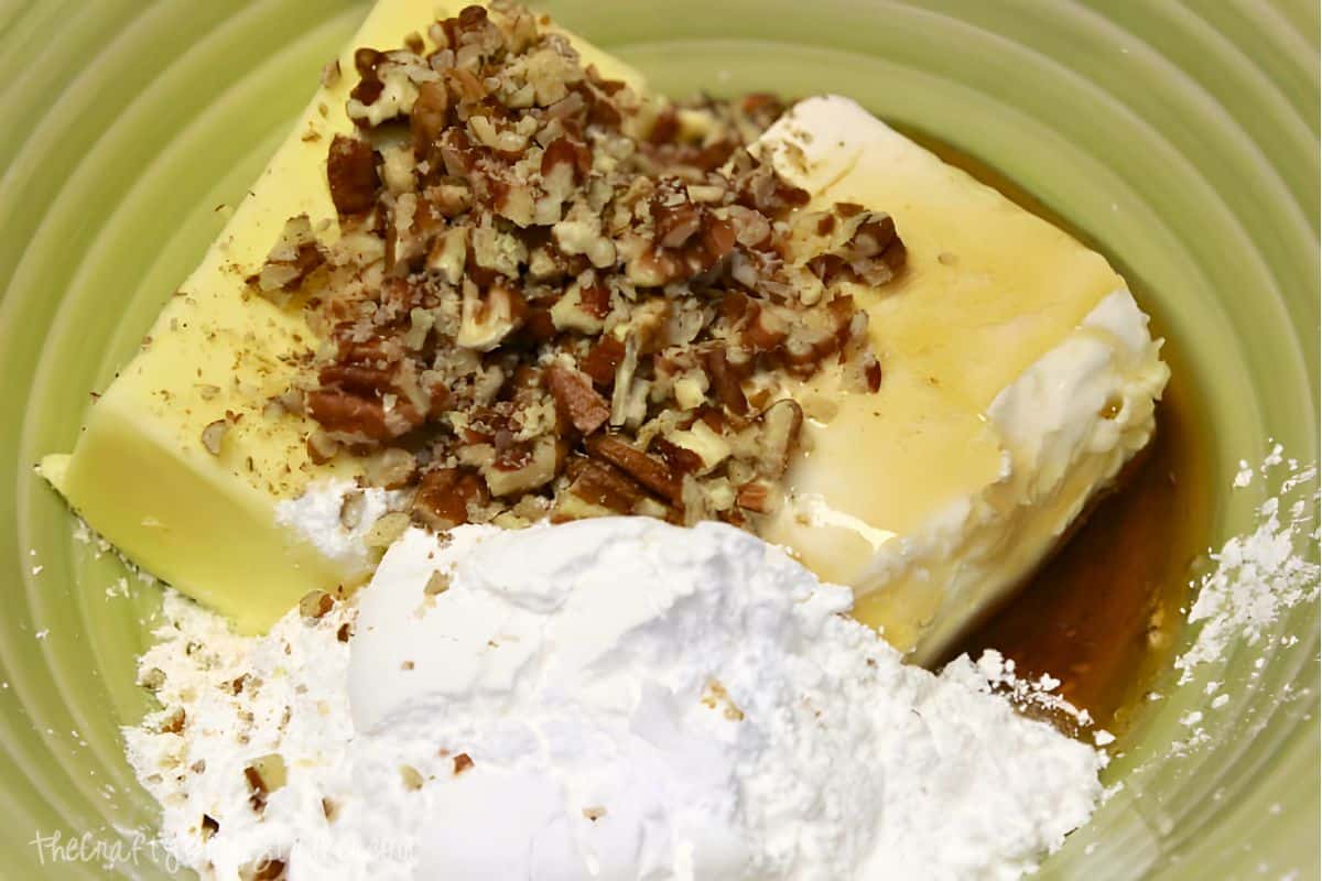 Butter, cream cheese, chopped pecans, powdered sugar, and syrup in a bowl.