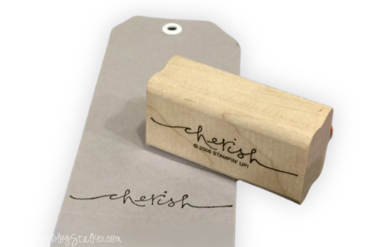 A kraft paper tag with a white eyelet, stamped with the word "cherish" using a wooden rubber stamp, creating a simple and elegant design for crafting or gifting.