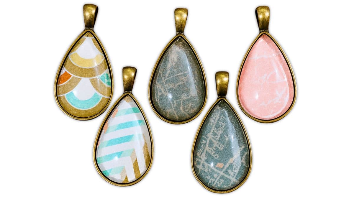 Five teardrop pendants with bronze trays, each featuring different patterned paper designs sealed under clear glass cabochons.