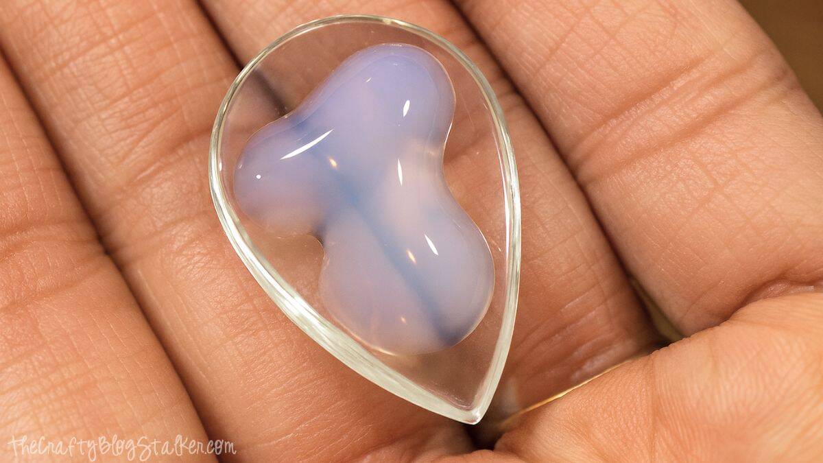 A hand holds a clear teardrop glass cabochon with diamond glaze, to create a unique pendant necklace. 