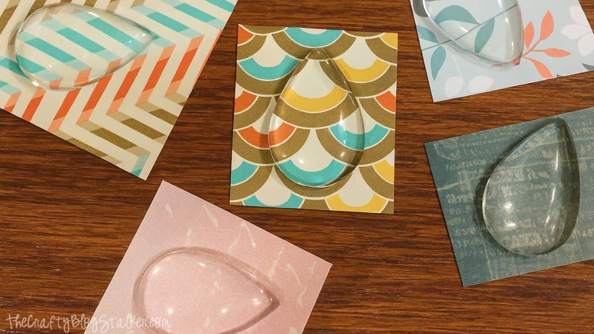Clear teardrop glass cabochons placed over colorful patterned scrapbook paper squares, ready for making custom jewelry designs.
