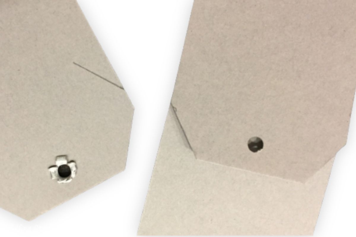Close-up of two kraft paper tags, one with a metal eyelet and the other with a punched hole, featuring traced slit lines for precise cuts in a DIY project.