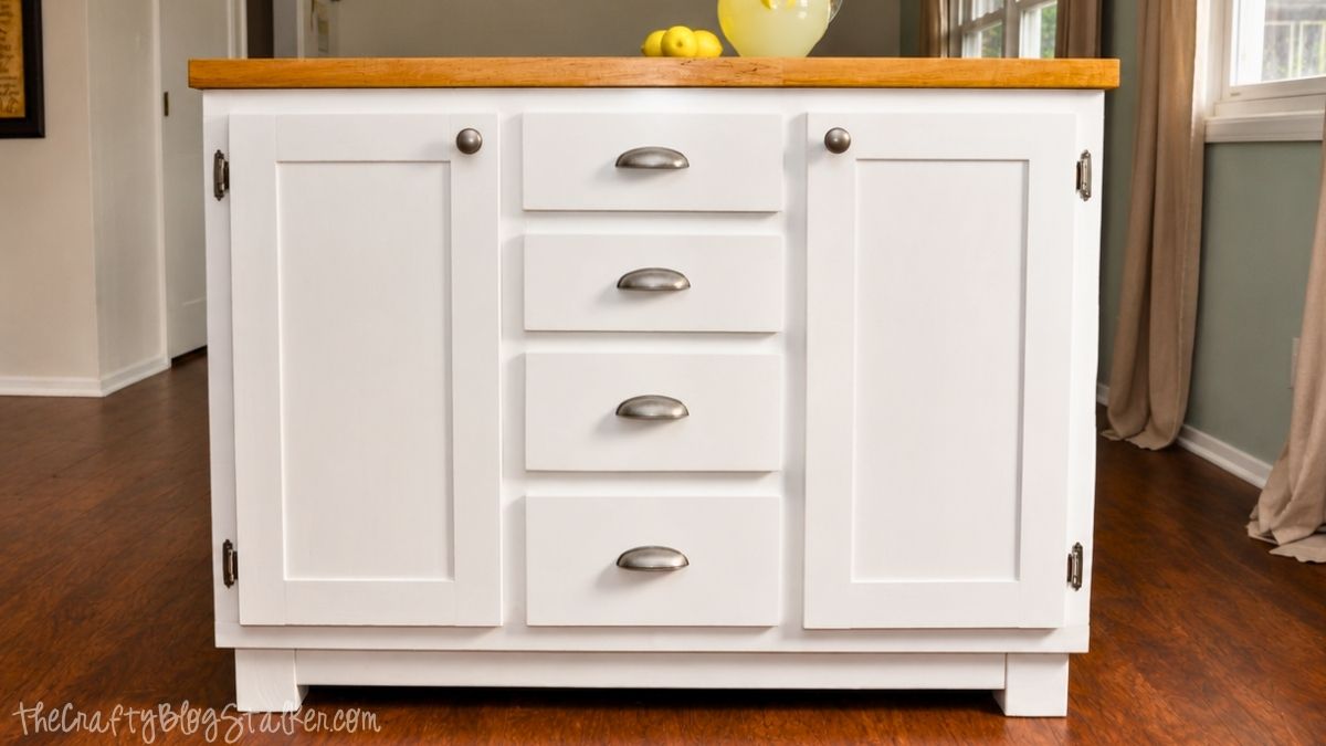 White DIY kitchen island with drawers, cabinet doors, silver hardware, and a wood countertop on hardwood floors.
