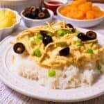 Plate of Hawaiian haystacks with creamy chicken over white rice, topped with chow mein noodles, black olives, and green onions.