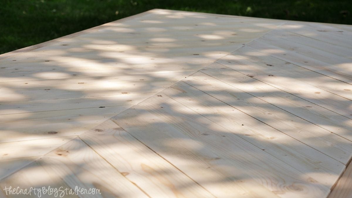 Close-up of a handmade wooden farmhouse table top featuring a herringbone pattern made from unfinished wood planks.