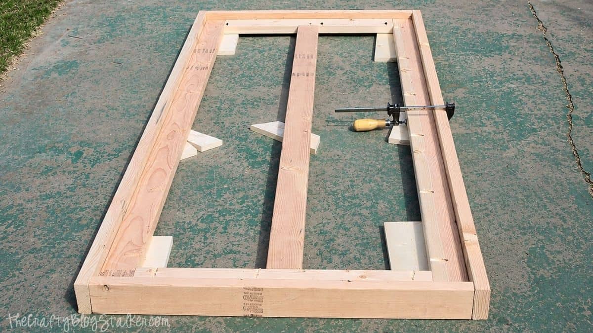 Wooden farmhouse table frame with trim boards and clamps arranged on a concrete patio during a DIY table build.