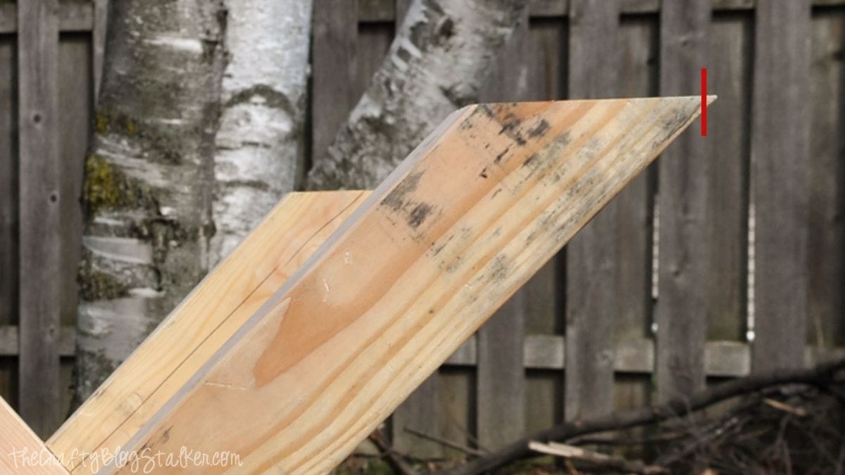 Close-up of a wooden farmhouse table leg marked for trimming with an angled cut during a DIY table building project.