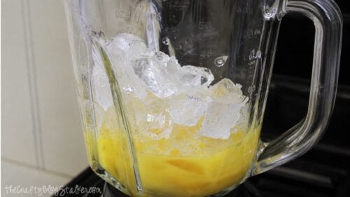 Ice cubes and orange juice concentrate added to a blender pitcher for making a homemade orange juice slushie.