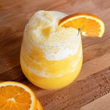 Homemade orange juice slushie in a glass with a frothy frozen texture, garnished with a fresh orange slice.