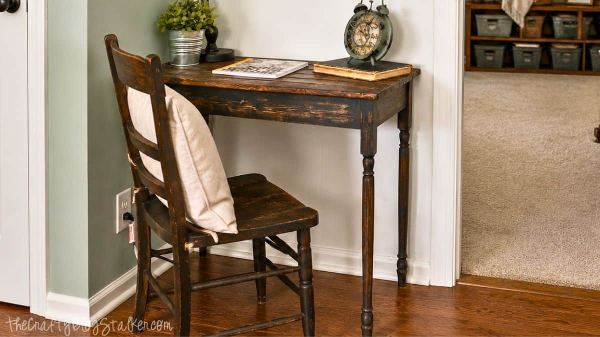 Rustic wooden writing table with a matching chair, books, clock, and small plant in a cozy hallway corner.