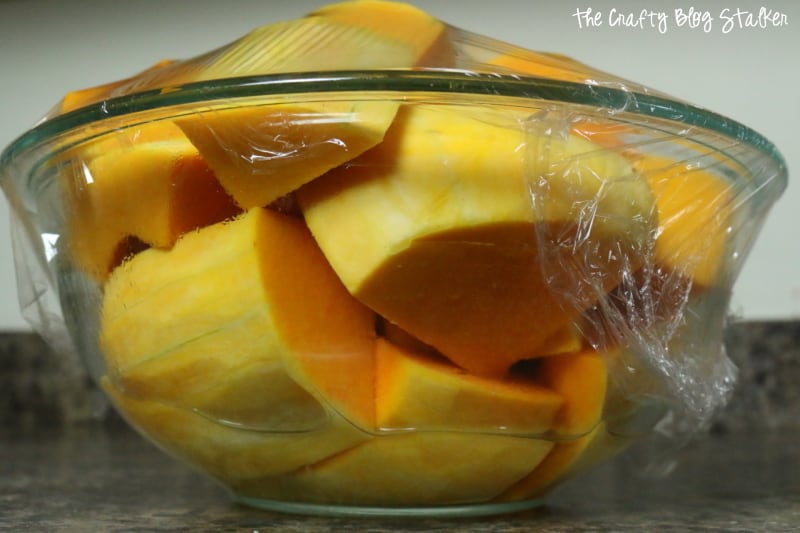 a bow of cut butternut squash in a microwave safe bowl and plastic wrap over the top