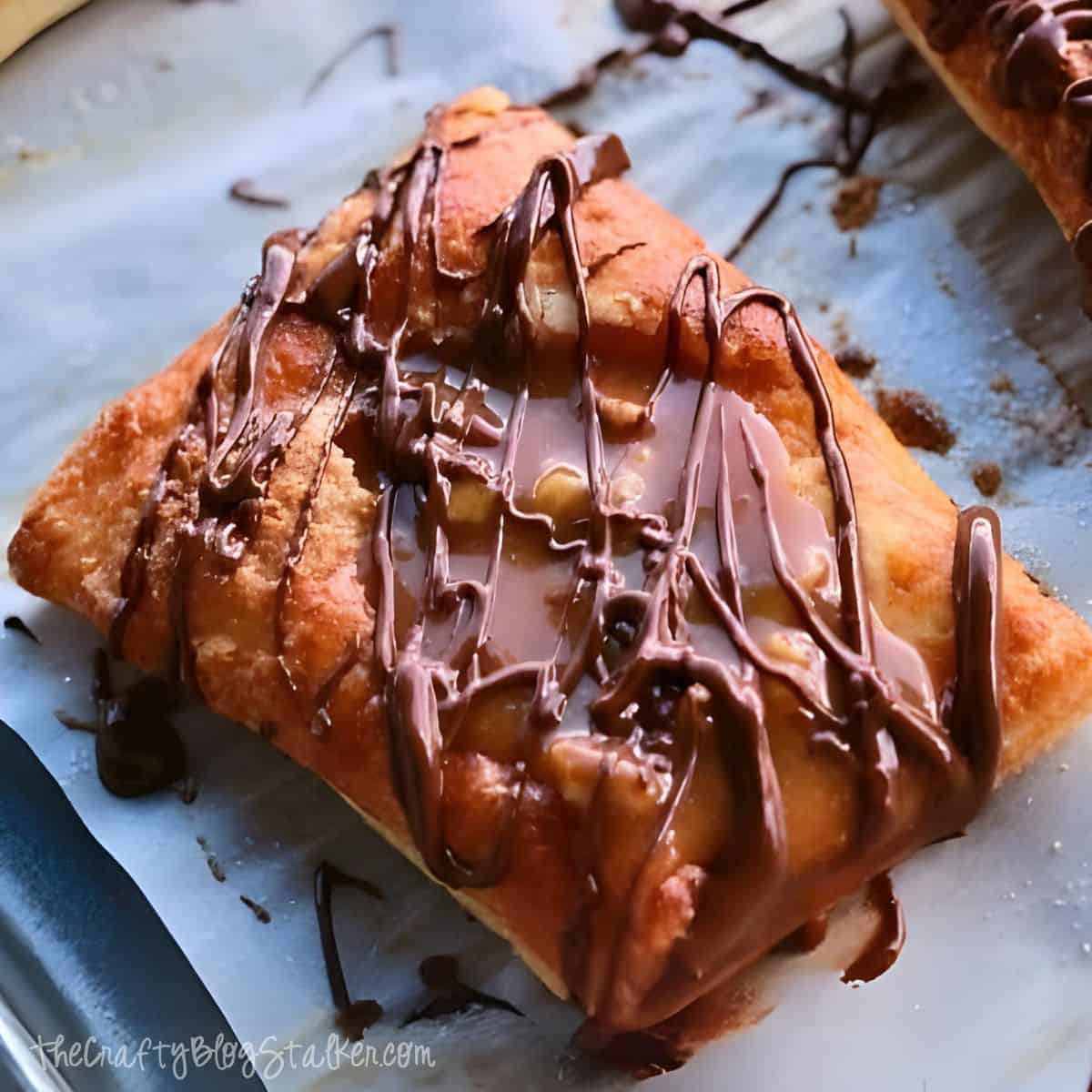 Golden puff pastry topped with gooey caramel, crunchy pecans, and drizzles of rich melted chocolate, creating a decadent dessert with a satisfying mix of textures and flavors.