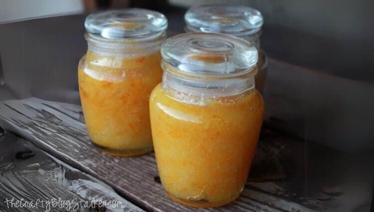 Three small glass jars filled with homemade orange sugar scrub sitting on a rustic wooden surface.