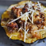 Close-up of roasted acorn squash filled with sausage, apples, onions, and breadcrumbs, topped with shredded Parmesan cheese before baking.
