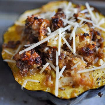 Close-up of roasted acorn squash filled with sausage, apples, onions, and breadcrumbs, topped with shredded Parmesan cheese before baking.
