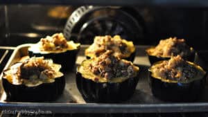 Stuffed acorn squash halves filled with sausage and apple stuffing baking on a sheet pan inside the oven until golden and heated through.