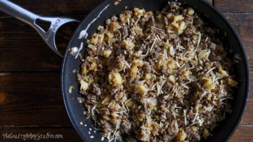 Skillet filled with cooked sausage, diced apples, onions, breadcrumbs, and Parmesan cheese for stuffing roasted acorn squash.