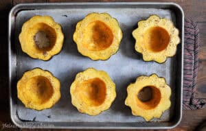 Roasted acorn squash halves seasoned with salt and pepper on a baking sheet, ready to be filled with sausage and apple stuffing.