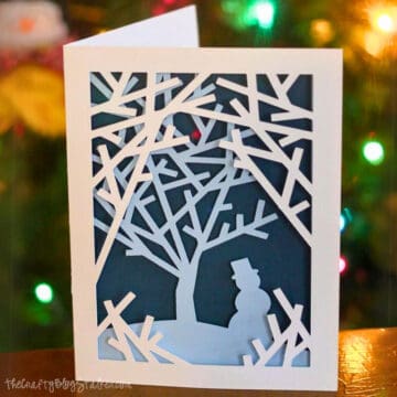 Finished layered snowman card in front of Christmas lights.