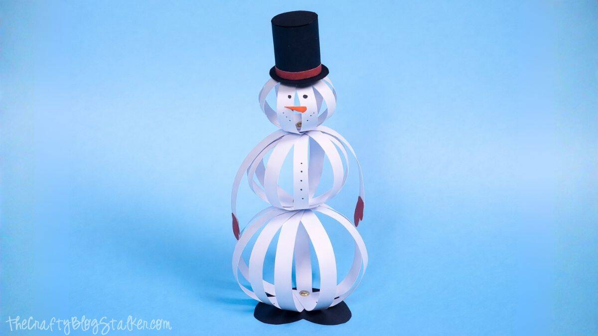 Finished paper strip snowman standing upright with a top hat, carrot nose, coal face details, paper strip body, mittens, and boots on a solid background.