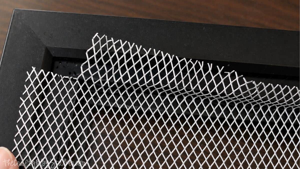 Metal mesh being fitted into a black picture frame, with edges bent to shape inside the frame.