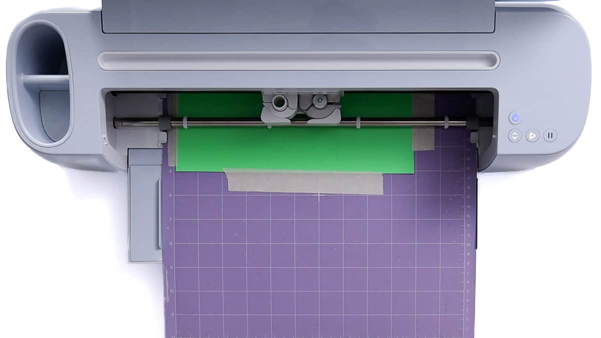 A Cricut machine cutting a sheet of Super Pop HTV placed on a purple StrongGrip mat, secured with tape along the edges.